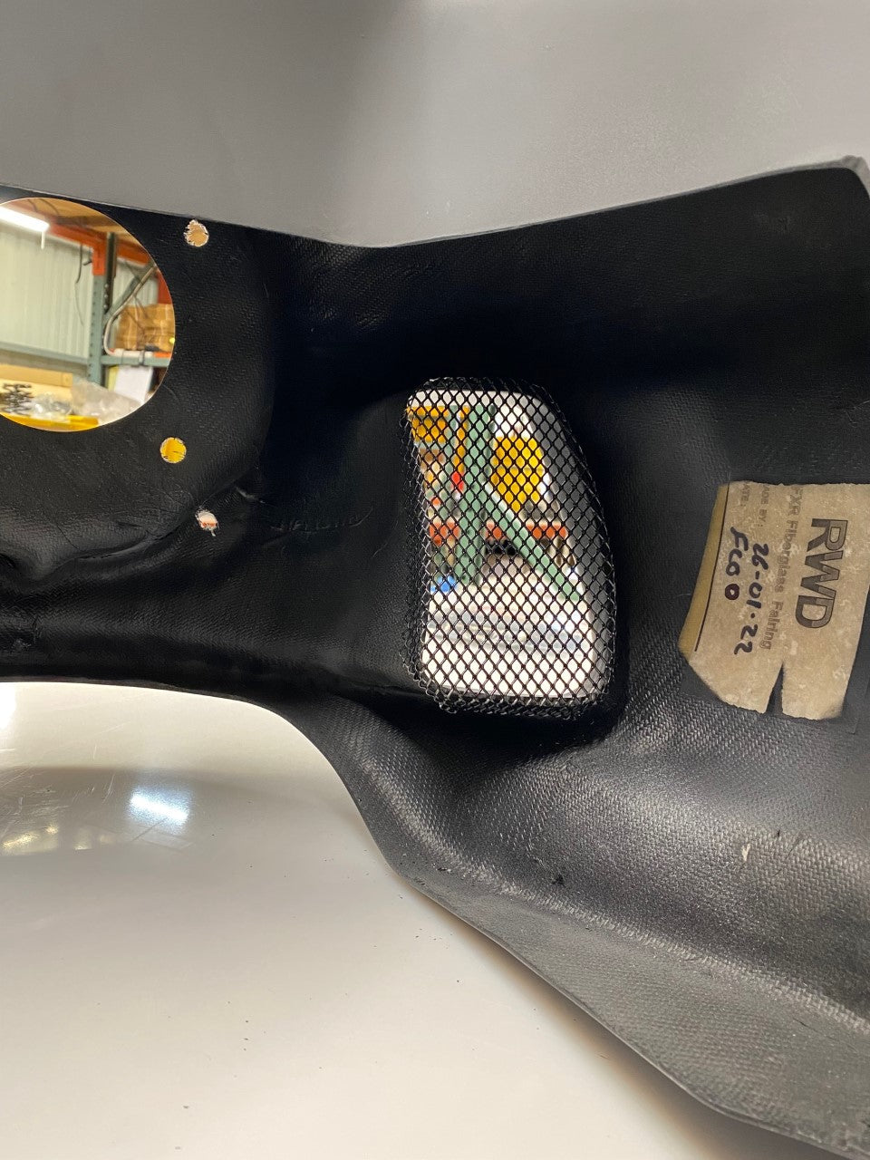 RWD V-Twin black textured fiberglass or carbon fiber part with a mesh-covered opening revealing internal components, and a circular opening.